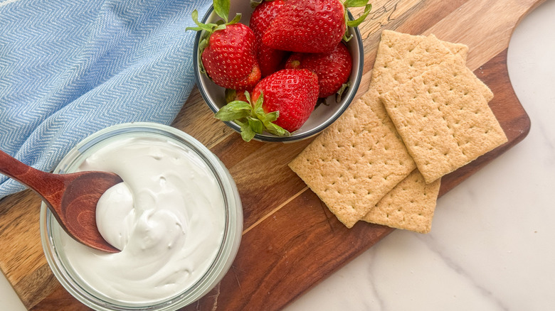 jar of marshmallow fluff on board with strawberries and graham crackers