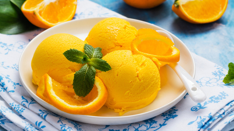 Orange sherbet on a white plate with fresh mint and orange slices