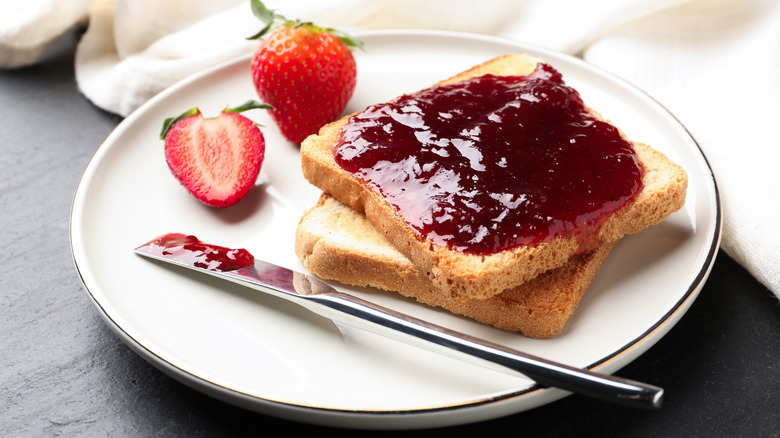 Toast with strawberry jam alongside fresh strawberries and a knife with a dab of jam on it