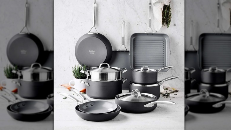 GreenPan pots, pans, and griddle stacked on a white counter against a white wall with herbs