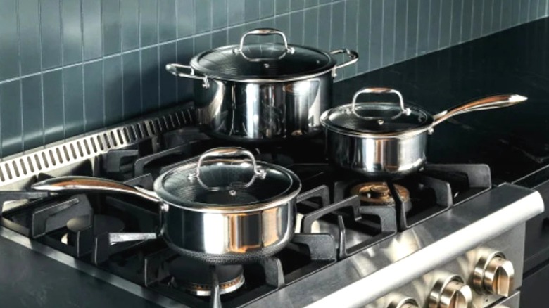 Three HexClad pots and lids sitting on a gas stovetop
