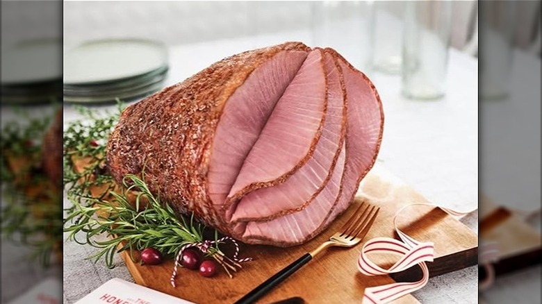 Partially sliced Honey Baked Ham on cutting board with fork and garnish.