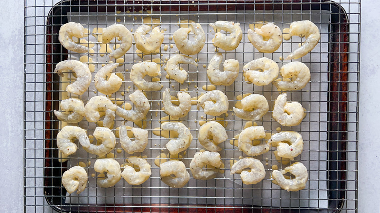 Battered shrimp on rack over baking sheet