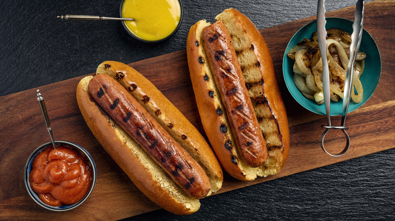 Grilled hot dogs on wooden board with toppings on the side