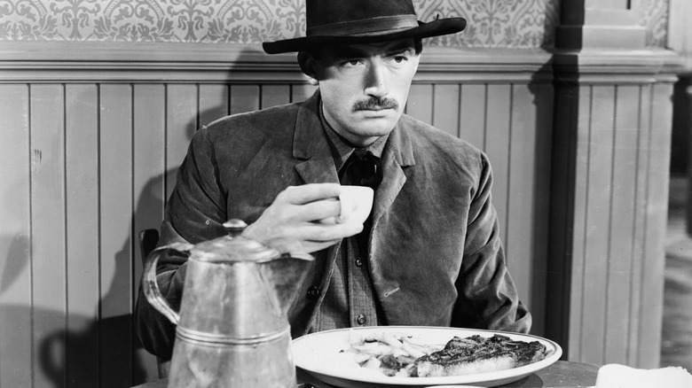 Gregory Peck holding a mug and eating steak