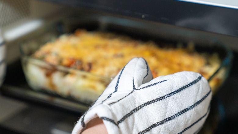 Person wearing an oven mitt pulling a casserole in a glass dish out of the oven.