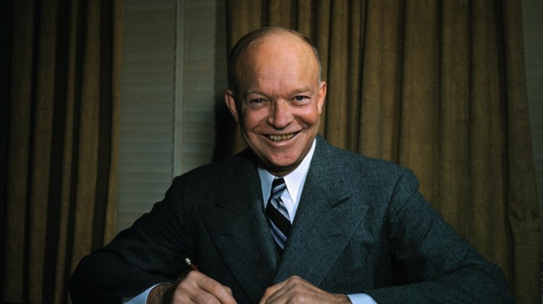 Dwight D. Eisenhower smiling while sitting down holding a pen