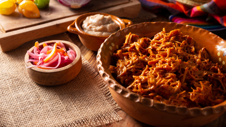 stewed pork from Mexico surrounded by garnishes on rustic background