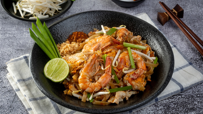 A bowl of pad thai sitting upon a cloth napkin.