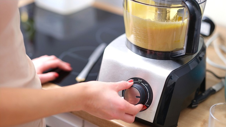 A hand turning the dial of a food processor filled with cake batter.