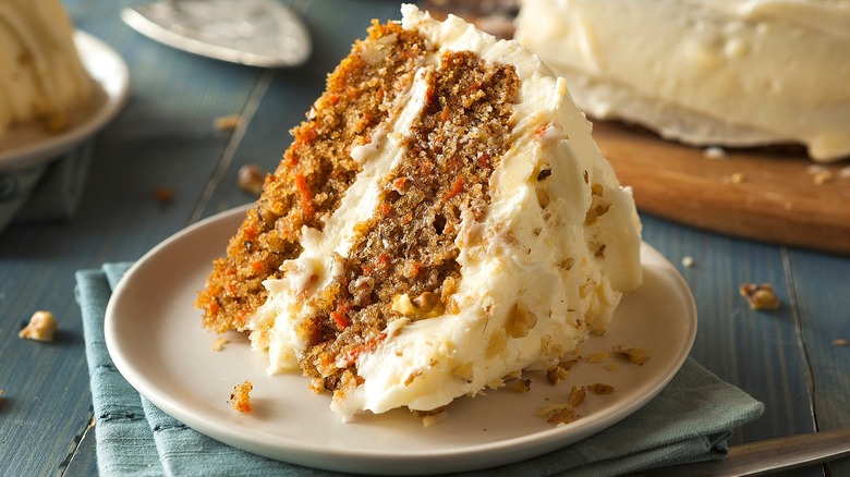One slice of two-layer carrot cake with cream cheese frosting on a small cream-colored plate.