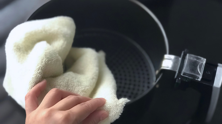 Person's hand wiping an air fryer basket with a towel