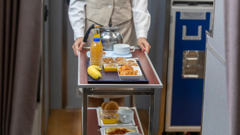 Flight attendant wheeling cart of food on plane
