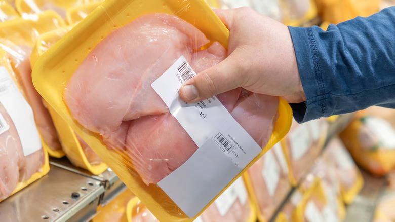 Hand taking a package of chicken breasts off of a shelf