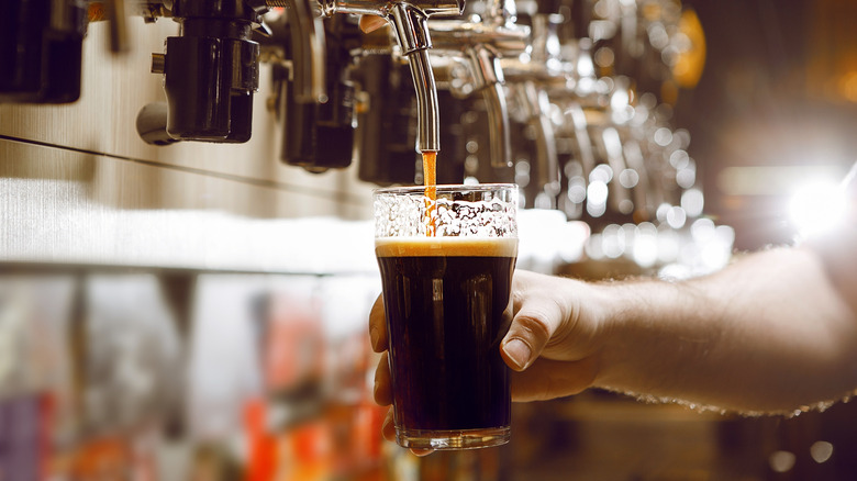 Person pouring stout beer in a glass from the tap