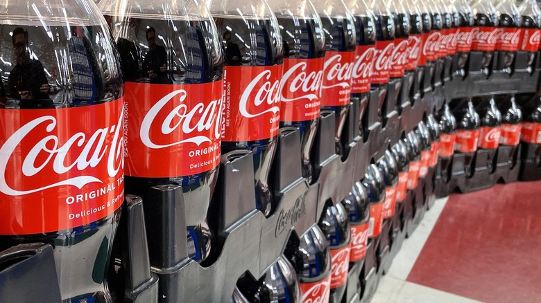 A row of 2-liter Coke bottles lines a grocery store wall