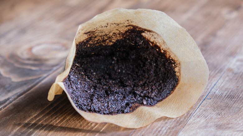 Used coffee grounds in a coffee filter on wood surface.