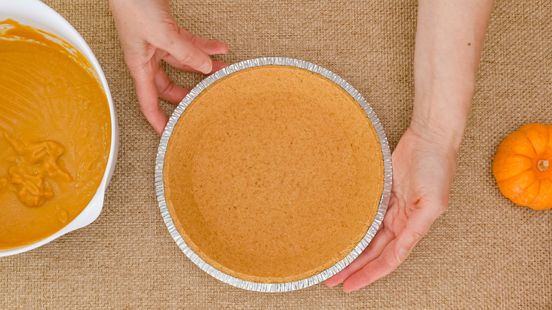 Hands touching pumpkin pie in a disposable pie pan