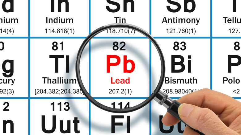 Hand holding a magnifying glass over the periodic table on Pb (lead)