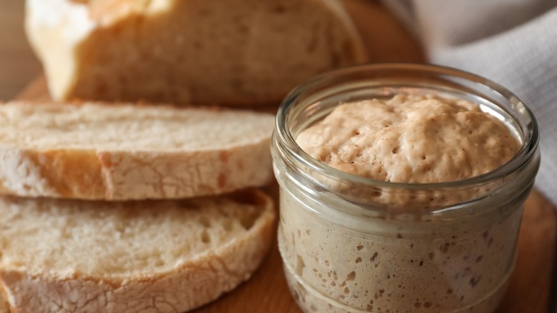 A jar of sourdough starter sits next to sourdough bread