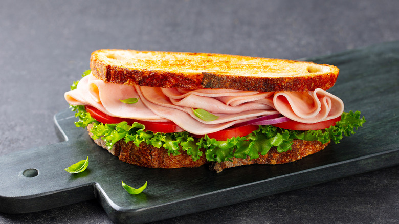 Ham, tomato, and lettuce sandwich on a gray cutting board