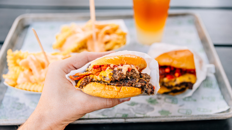 Person holding generic fast food sandwich with fries in background