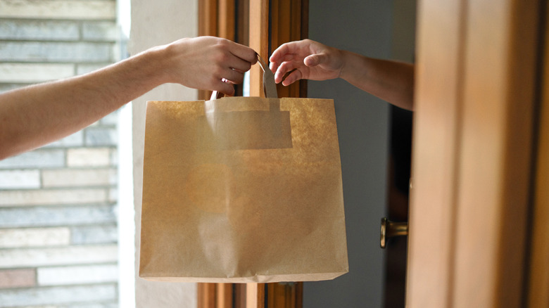 A hand passing a brown paper bag to another at the doorstep