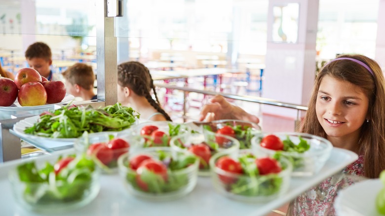 Girl taking salad bowl from cafeteria counter.