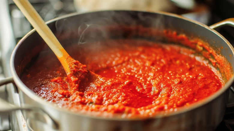 A pan of hot tomato sauce cooking on a stove, stirred with a wooden spoon.