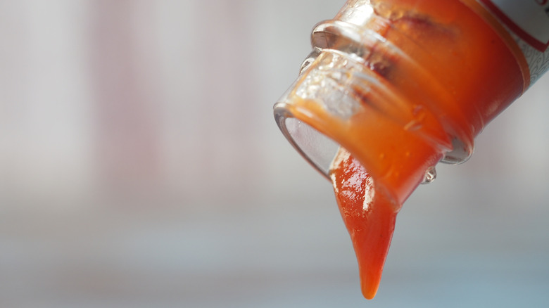 Pouring last bits of ketchup from a bottle.