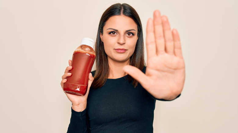Woman holding up hand indicating "stop" while holding a bottle of ketchup.