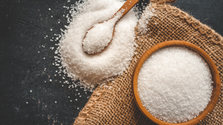 A bowl of salt crystals next to a pile of salt with a wooden spoon