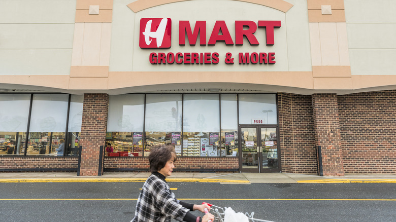 A person pushing a shopping cart in front of an H Mart store.