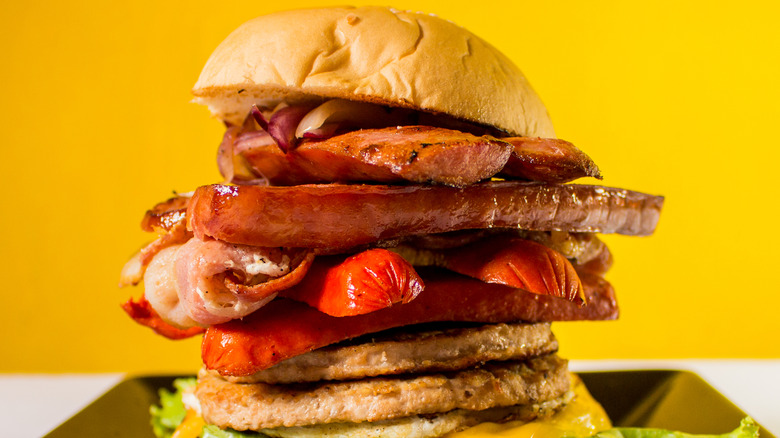 A massive X-Tudo with various types of meat, vegetables, and toppings in a very tall stack