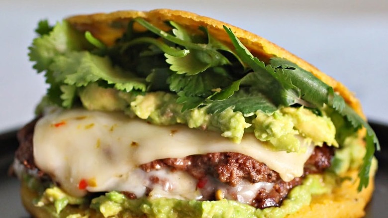 A burger patty with cheese and lettuce stuffed inside an open arepa