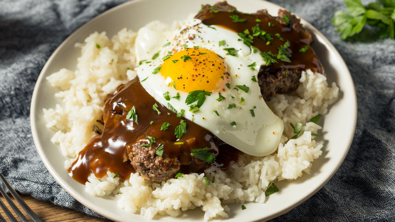 A loco moco featuring a rice, a burger patty, gravy, and a fried egg