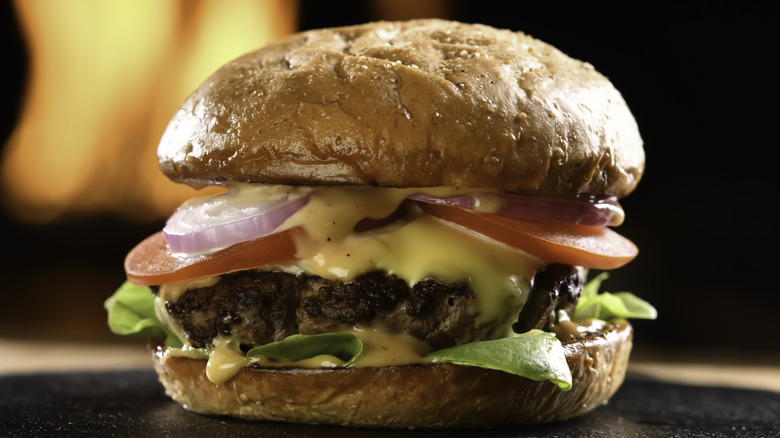 A classic burger on a stone plate with a dark, flame-lit background