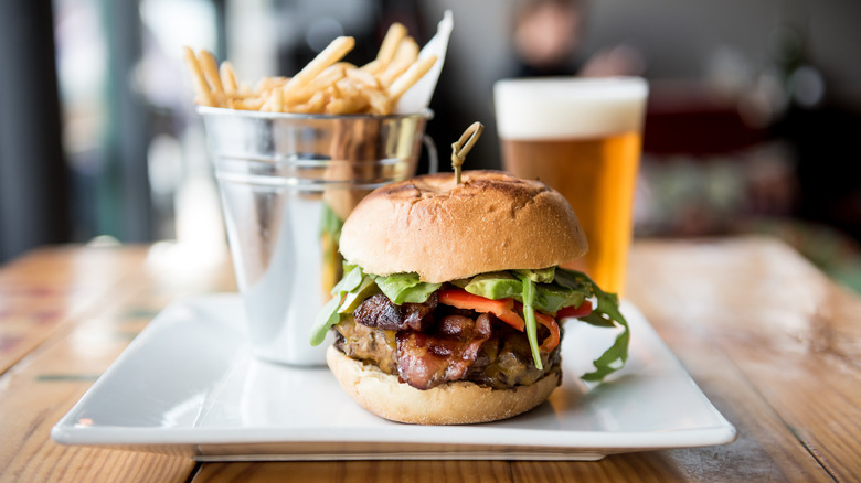 A thick-pattied burger on a plate served with fries and a beer