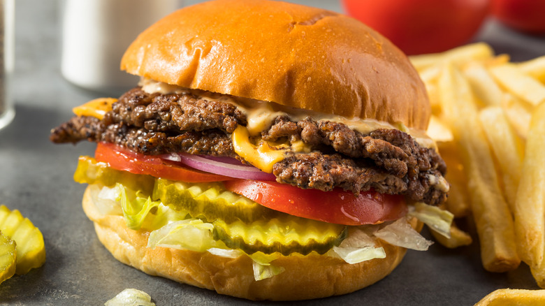 A double-patty smashburger with cheddar cheese, lettuce, tomato, pickles, and fries on the side