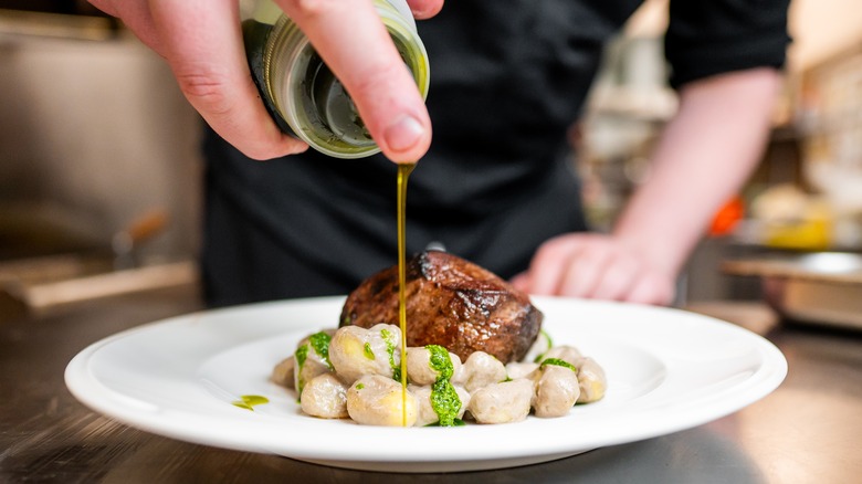 Chef drizzles olive oil on a plate of meat and pasta