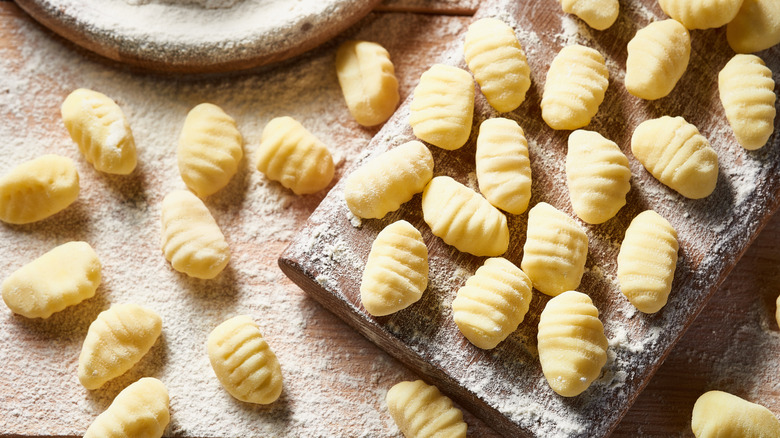 Raw potato gnocchi on a wooden board and a plate of flour.