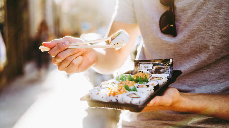 Person eating grocery store sushi with chopsticks