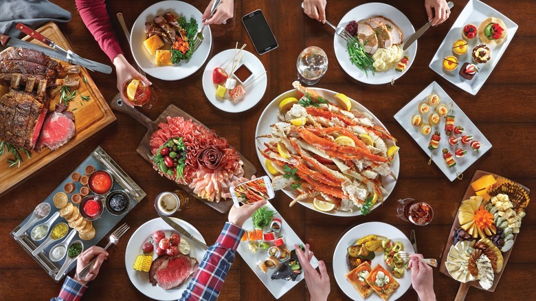 Overhead view of a table with sliced beef, crab legs, charcuterie boards, and other luxury dining items