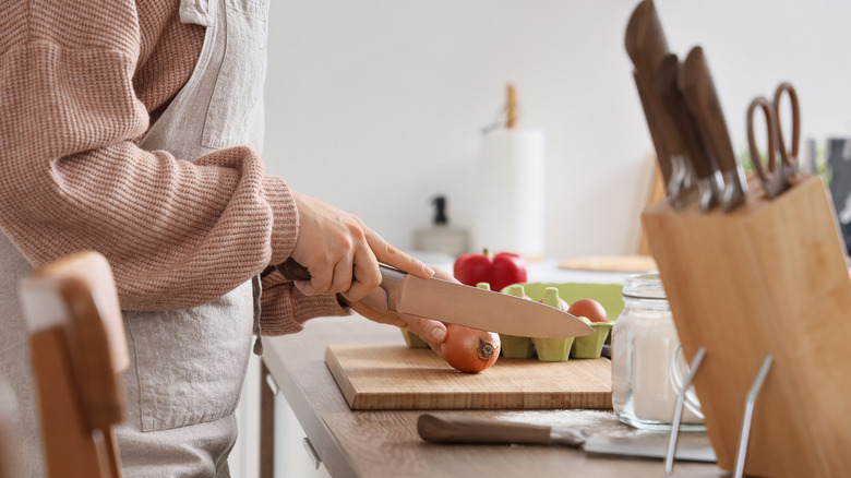 Person cutting an onion with a knife on a wooden cutting board