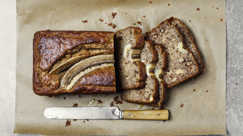 Banana bread sliced on parchment paper with knife.