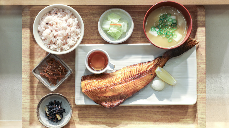 nampan kayu berisi semangkuk sup miso, nasi putih, ikan matang, saus celup, irisan lemon, dan berbagai sayuran