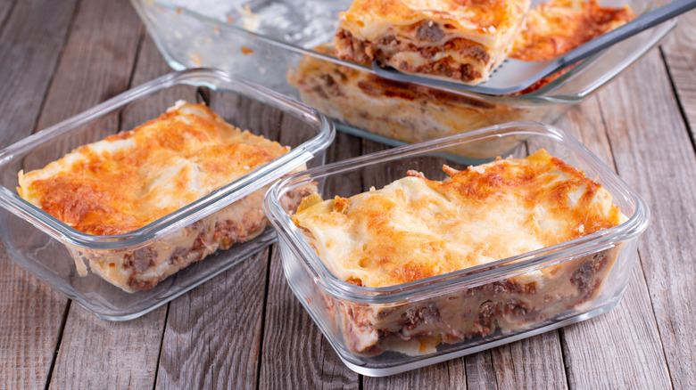 Portions of lasagna are placed in containers to freeze from a larger dish.