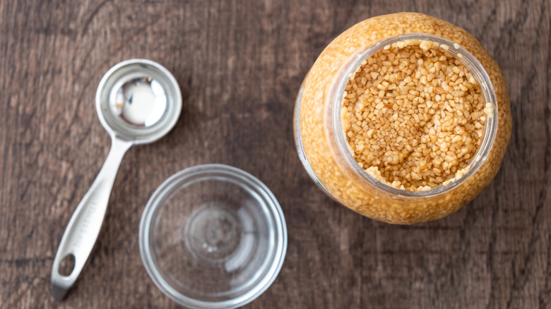 Overhead shot of open container of minced garlic next to a bowl and a spoon