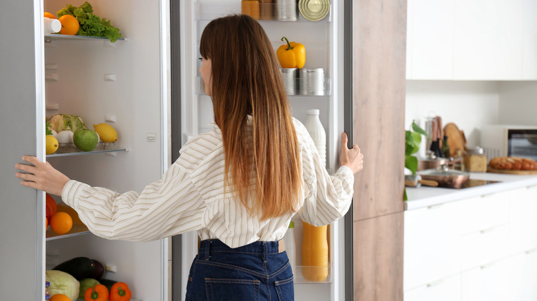 A woman looks at fresh vegetables inside her kitchen fridge