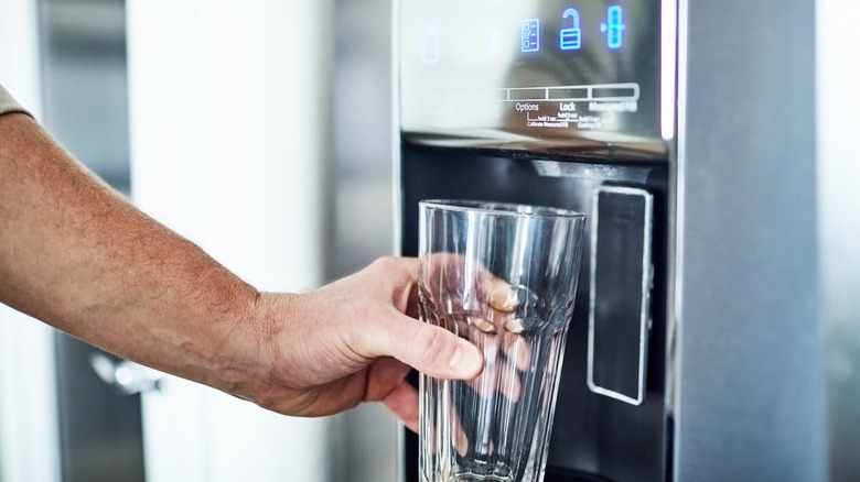 Person filling a glass from a refrigerator water dispenser